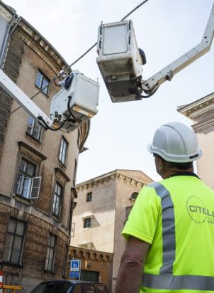 worker wearing a helmet and safety vest looking at a crane next to a building
