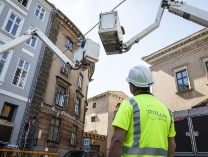 worker wearing a helmet and safety vest looking at a crane next to a building