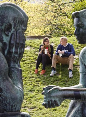 man and woman sitting on grass outside next to a status of man and woman in a park