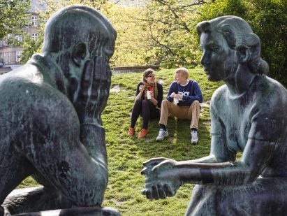 man and woman sitting on grass outside next to a status of man and woman in a park