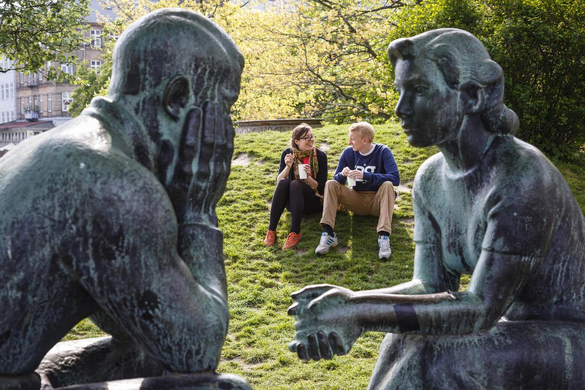 man and woman sitting on grass outside next to a status of man and woman in a park
