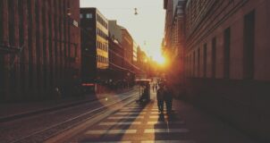 two people walking between concrete buildings towards sunshine
