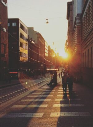 two people walking between concrete buildings towards sunshine
