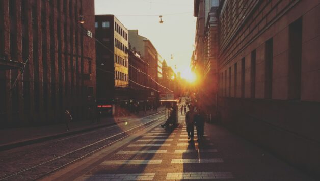 two people walking between concrete buildings towards sunshine