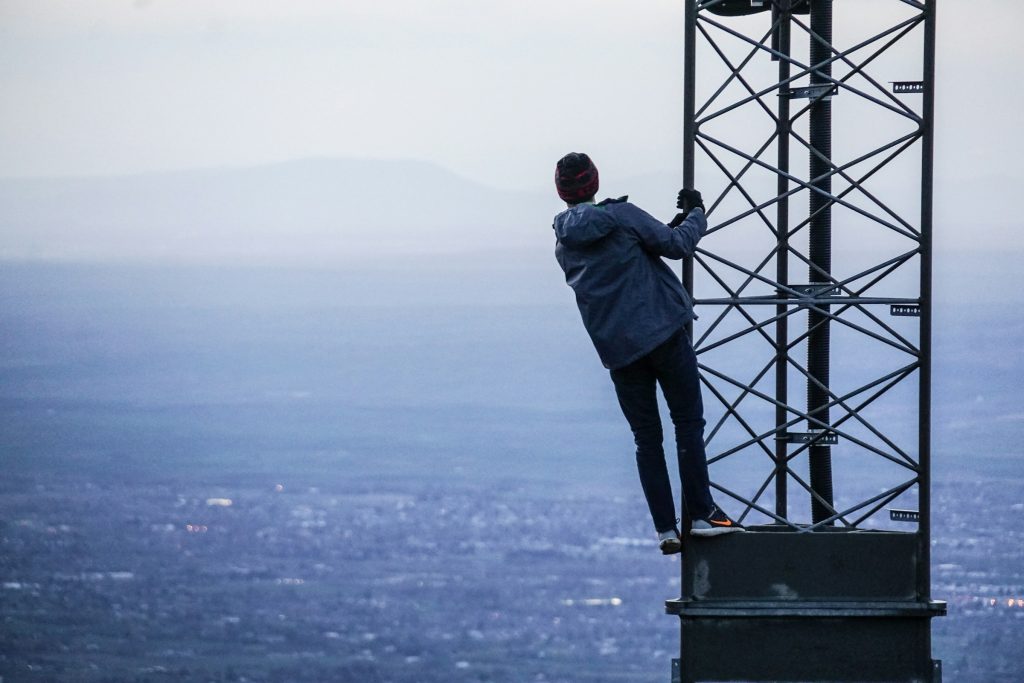 A person climbs a metal tower with a vast landscape in the background.